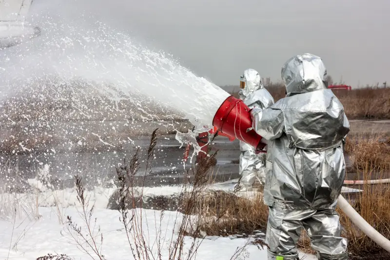 Firefighters wearing hazardous materials suits spraying fire-suppresant foam